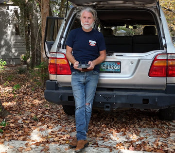Man standing next to a silver SUV in a forested area