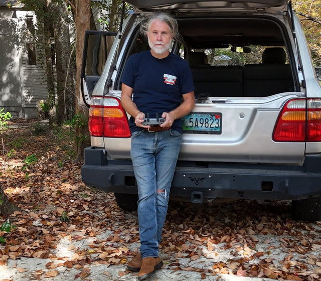 Man standing next to a silver SUV in a forested area