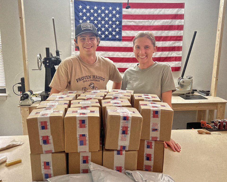 Two people sitting behind a stack of boxes with American flag in the background
