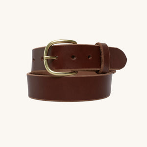 Brown full grain leather belt with a solid brass round buckle, styled in a classic loop against a plain light background.