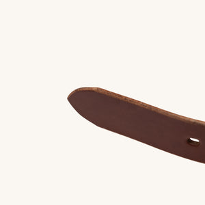Close-up view of the pointed tip and burnished edge of a brown full grain leather belt.